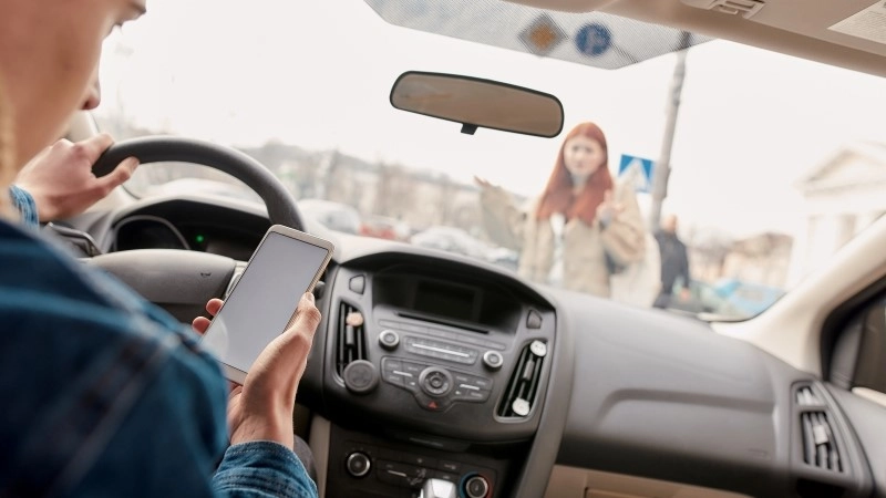 Distracted young male driver looking at the screen of his mobile phone while running over a pedestrian.
