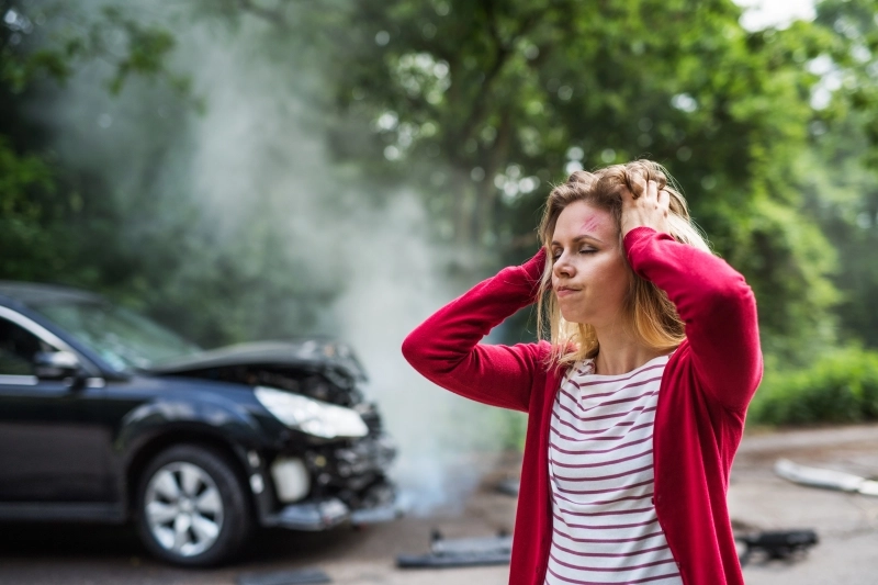 An injured young woman standing by the damaged car after a car accident.