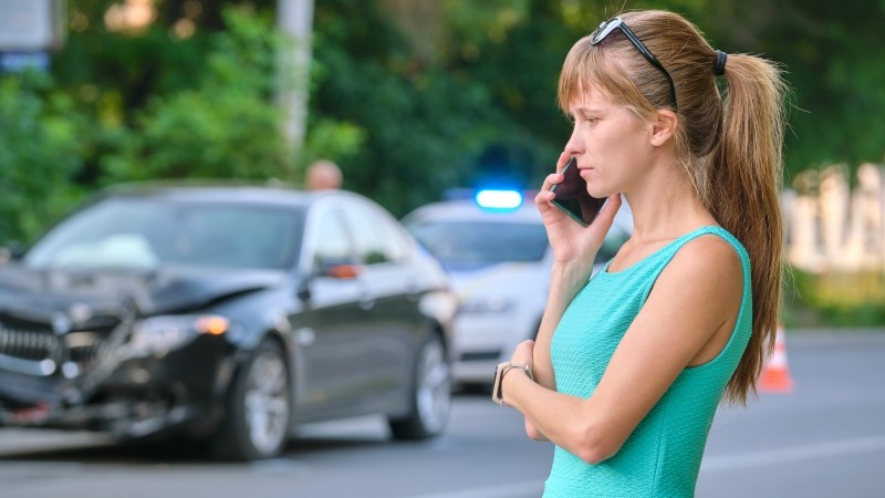 Stressed woman driver talking on mobile phone on street side calling for emergency service after car accident. Road safety and insurance concept.