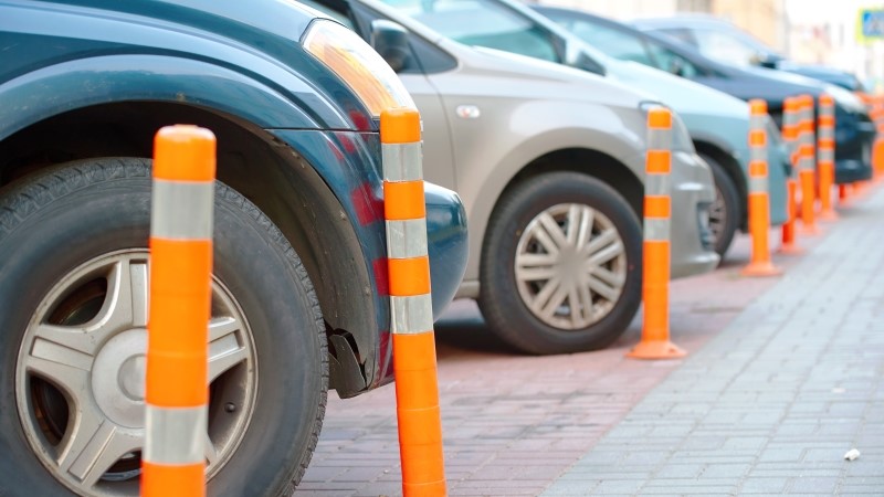 Car makes contact with plastic bollard, leaving scratches and minor damage on the vehicle's bumper. Car parked close to orange reflective bollard.