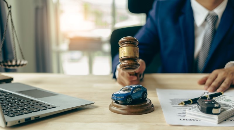 judge's gavel and miniature car as symbols of auction or court action against driver who got into an accident and received car insurance money on the table.