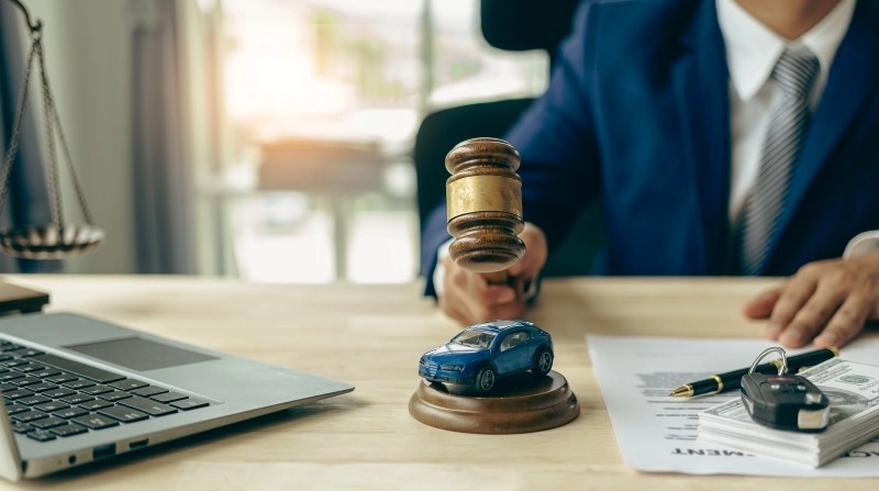 judge's gavel and miniature car as symbols of auction or court action against driver who got into an accident and received car insurance money on the table.
