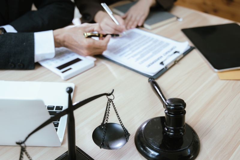 Close up of male lawyer working with contract documents and wooden hammer on table in courtroom.