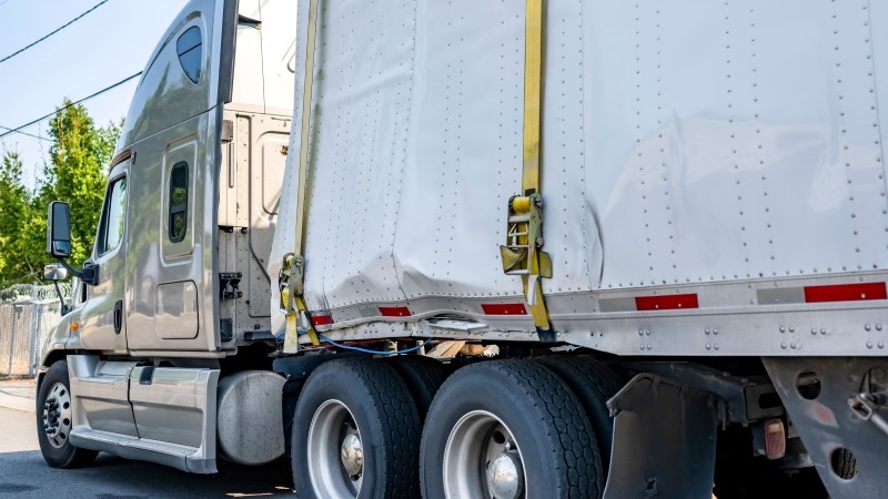 Beige industrial grade big rig semi truck tractor with broken dry van semi trailer
