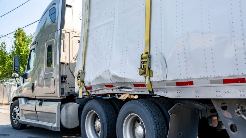 Beige industrial grade big rig semi truck tractor with broken dry van semi trailer