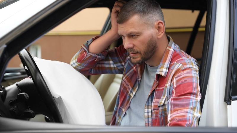 Injured man near opened airbag in automobile after car accident