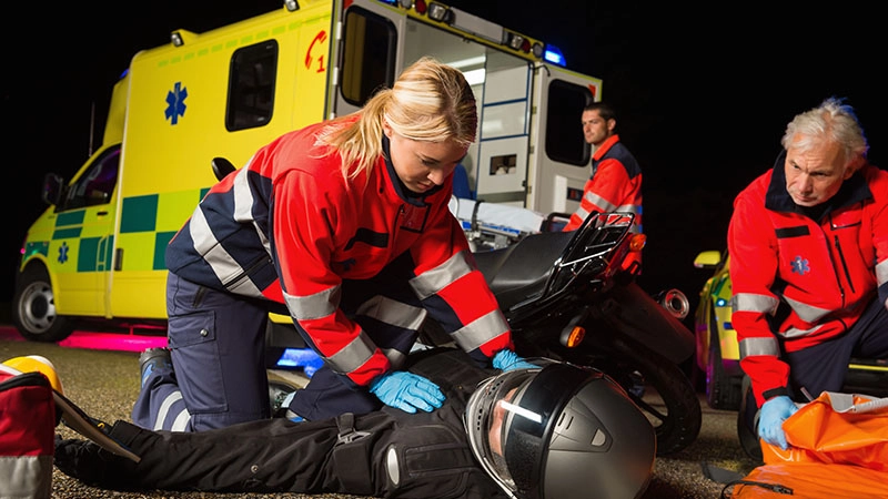 Paramedics treating injured motorcyclist beside ambulance at nighttime crash scene