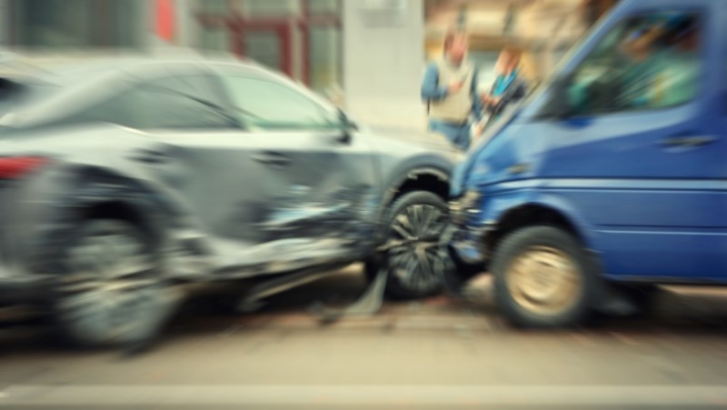 Blurred motion image of car crash scene in city street involving blue van and silver car, chaotic aftermath of an urban traffic accident.