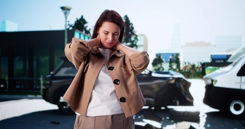 Woman clutching neck beside damaged vehicles after traffic collision