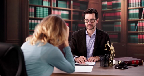 distressed woman meeting with attorney at desk beside scales of justice statue