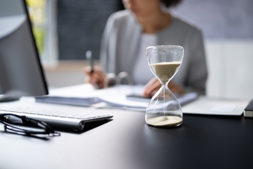 hourglass on office desk with professional reviewing documents in background
