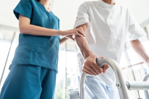 nurse in scrubs assisting patient using metal walker during physical therapy