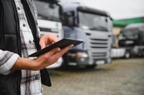 fleet manager holding digital tablet standing in front of commercial trucks
