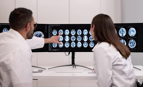 two physicians in lab coats reviewing brain MRI scans on large monitors