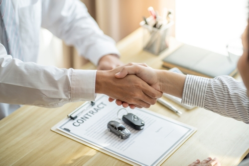Handshake over contract clipboard with toy car and car key on desk