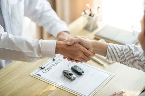Handshake over contract clipboard with toy car and car key on desk