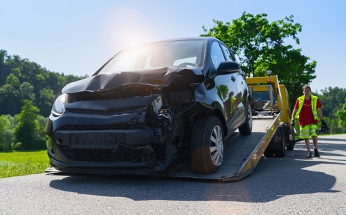 severely damaged vehicle loaded onto flatbed tow truck by roadside worker