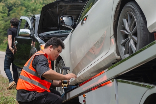 tow truck operator securing damaged vehicle onto flatbed tow truck
