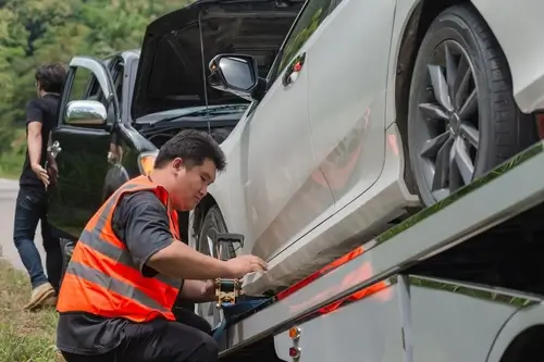 tow truck operator securing damaged vehicle onto flatbed tow truck